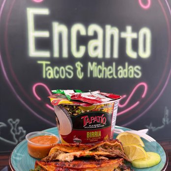 Birria-flavor ramen cup with toppings, served alongside crispy quesabirria tacos, salsa, and lime on a teal plate