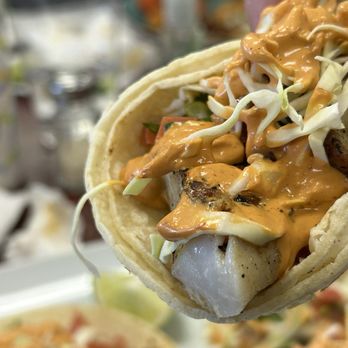 Close-up of a taco held up to the camera, topped with cabbage, crema, and pico de gallo