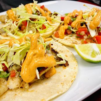 Three tacos on corn tortillas piled with shredded cabbage, pico de gallo, and a swirl of chipotle crema