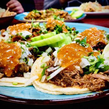 Plate of street tacos topped with onions, cilantro, and salsa, garnished with cucumber slices